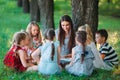 Children and education, young woman at work as educator reading book to boys and girls in park. Royalty Free Stock Photo