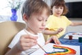 Children engaged in creativity in the home interior. Child draws and colors the picture with paints and a brush