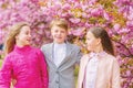 Children enjoy warm spring. Lost in blossom. Girls and boy friends posing near sakura. Kids on pink flowers of sakura