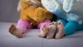 Children feet closeup, multiracial friends sitting on sofa, playing with teddies