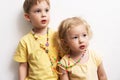 Children girl and boy in yellow T-shirts and bright beads against the background of a white wall. Interested look away.