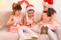 Children girls portrait, sisters dressed in santa helper hat, sitting on a couch in home interior decorated with christmas lights