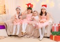 Children girls portrait, sisters dressed in santa helper hat, sitting on a couch in home interior decorated with christmas lights