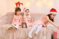 Children girls portrait, sisters dressed in santa helper hat, sitting on a couch in home interior decorated with christmas lights