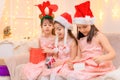 Children girls portrait, sisters dressed in santa helper hat, sitting on a couch in home interior decorated with christmas lights