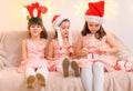 Children girls portrait, sisters dressed in santa helper hat, sitting on a couch in home interior decorated with christmas lights