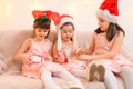 Children girls portrait, sisters dressed in santa helper hat, sitting on a couch in home interior decorated with christmas lights