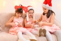 Children girls portrait, sisters dressed in santa helper hat, sitting on a couch in home interior decorated with christmas lights