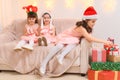 Children girls portrait, sisters dressed in santa helper hat, sitting on a couch in home interior decorated with christmas lights