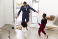 Children Greeting And Hugging Working Businessman Father As He Returns Home From Work