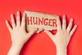 Children hands holding cardboard with text Hunger on red background. Food crisis, global hunger, food supply issue Royalty Free Stock Photo