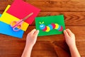 Children hands holding paper applique caterpillar. Paper sheets, scissors on a brown wooden background Royalty Free Stock Photo
