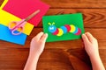 Children hands holding paper applique caterpillar. Paper sheets, scissors on a brown wooden background Royalty Free Stock Photo