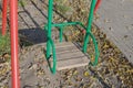 Children hanging swing with  battered wooden seat, green metal frame and red posts against gray ground with dry autumn leaves Royalty Free Stock Photo