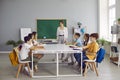 Happy students sitting around table in classroom, reading books and talking with teacher Royalty Free Stock Photo