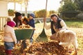 Children Helping Parents To Collect Autumn Leaves In Garden