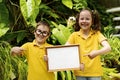 Children hold a white lettering sheet against a background of green leaves