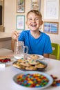 Funny boy eat cookies with round multi-colored sweets and drink milk. Royalty Free Stock Photo