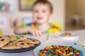 Funny boy eat cookies with round multi-colored sweets m&m and drink milk. Royalty Free Stock Photo