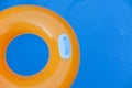 Children inflatable orange swimming ring with white handles floating in blue pool. Top view, close-up. Copy space for text