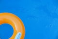 Children inflatable orange swimming ring with white handles floating in blue pool. Top view, close-up. Copy space for text