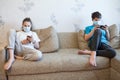 Children keep distance while using smartphones, kids wearing facial mask at home during coronavirus pandemic
