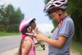 Children learn to ride bicycle in a park on summer day. Teenager boy helping preschooler girl to put on safety helmet Royalty Free Stock Photo