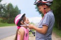 Children learn to ride bicycle in a park on summer day. Teenager boy helping preschooler girl to put on safety helmet Royalty Free Stock Photo