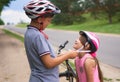 Children learn to ride bicycle in a park on summer day. Teenager boy helping preschooler girl to put on safety helmet Royalty Free Stock Photo