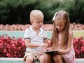 Children learning a digital tablet and sitting in the park. A boy and girl playing in a gadget on a natural background.