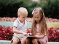 Children learning a digital tablet and sitting in the park. A boy and girl playing in a gadget on a natural background.