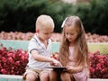 Children learning a digital tablet and sitting in the park. A boy and girl playing in a gadget on a natural background.