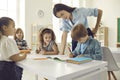 Young school teacher helping her little students who are writing in their notebooks Royalty Free Stock Photo