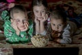 Children looking at laptop with cartoons showing before sleeping in bed. Three kids in bed watching a movie on a laptop and eating Royalty Free Stock Photo