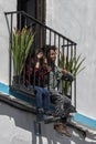 A boy and a girl are sitting on the floor of a balcony and stick their legs out between the bars of the railing.