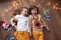 Children lying, laughing, have fun with Christmas decor, garland of light bulbs. Beautiful kids wearing sweater with deer