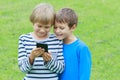 Children with mobile phone outdoor. Two boys smiling, looking to screen, playing games or using application. Technology Royalty Free Stock Photo