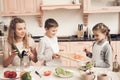 Children with mother in kitchen. Mother is helping kids prepare vegetables for salad. Royalty Free Stock Photo