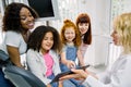 Children and mothers at dentist`s office. Two multiethnic mothers with their teen daughters, sitting in dentistry chair