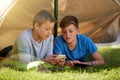 Children, phone and tent on grass for camping, virtual games and outdoor recreation on holiday. Young boys or kids and Royalty Free Stock Photo