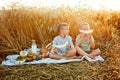 Children on a picnic in the countryside. The boys are sitting on a blanket with food in a wheat field. The child holds a slice of