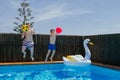 Two boys play with a ball and jump into a blue water pool.