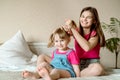 Children play on the bed in a bright bedroom. teen girl combing baby hair. funny girls. sisterly love. vacation home