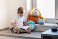 Children play a doctor. A large brown toy in a medical bandage and shoe covers is sitting on the window. A child is reading a book Royalty Free Stock Photo