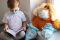 Children play a doctor. A large brown toy in a medical bandage and shoe covers is sitting on the window. A child is reading a book Royalty Free Stock Photo