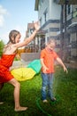 Children playing with garden sprinkler. Brother and sister running and jumping. Summer outdoor water fun in backyard