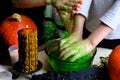 Children play with a green witchcraft potion, table is covered with a black cloth, pumpkins lie, animal skulls, candles are Royalty Free Stock Photo