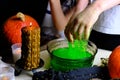 Children play with a green witchcraft potion, table is covered with a black cloth, pumpkins lie, animal skulls, candles are Royalty Free Stock Photo