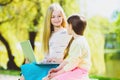 Children play laptop. Girls sitting against trees and lake outdoor