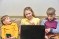 Children play on the phone and laptop. Two boys are sitting with a smartphone, and an older sister with a laptop Royalty Free Stock Photo